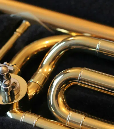 Close-up of shiny brass trumpet valves and tubing on a black fabric background with reflective golden finish