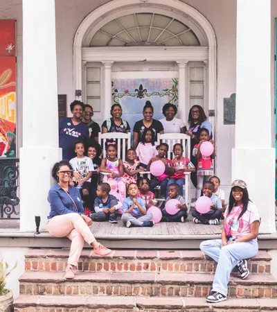 Group of adults and children posing with pink balloons on porch with colorful artwork on walls