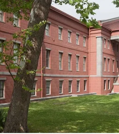 Red brick government building with white columns surrounded by green trees and lawn on a cloudy day.