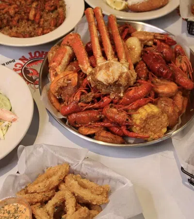 Seafood feast with crab, crawfish, fried shrimp, hush puppies, salad, and dessert on a white table.