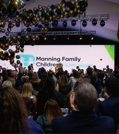 Audience applauding at a formal event with a large screen displaying Manning Family Children's LCMC Health