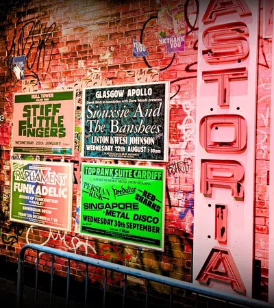 Graffiti-covered brick wall with vintage concert posters and neon Hysteria Theatre sign in a music venue.