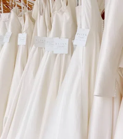 Row of elegant white wedding dresses hanging on wooden hangers in a bridal boutique.