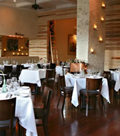 Elegant restaurant interior with white tablecloths, wooden chairs, candles, and polished hardwood floors