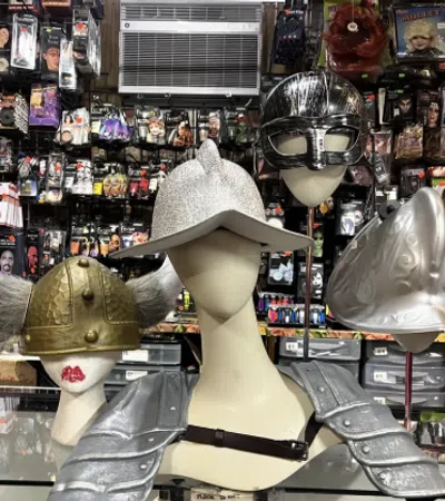 Display of medieval and Viking helmets on mannequins with costume store background of masks and wigs.