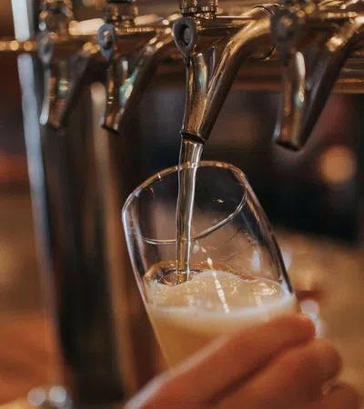 Beer being poured from a tap into a tilted glass at a bar with blurred background.