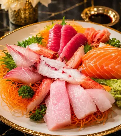 Assorted sashimi plate with salmon, tuna, white fish, crab, wasabi, and garnishes on a decorative plate.