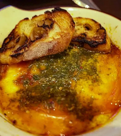 Baked melted cheese with herbs and oil served with crispy toasted bread slices in a rustic dish.