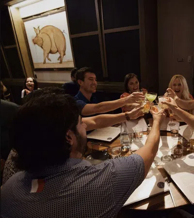 Group of friends raising glasses for a toast around a restaurant table with menus and drinks.