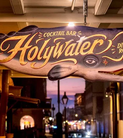 Hanging whale-shaped wooden sign for Holy Water oyster house, cocktail bar, and dining room at dusk.