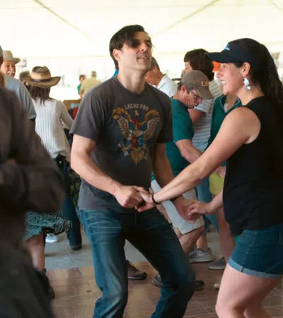 Couples dancing energetically in a lively indoor social dance event under a white tent