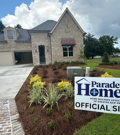 New brick home with landscaping and Parade of Homes official site sign in front yard under cloudy sky.