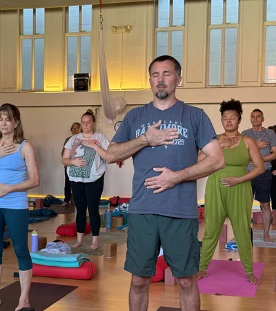 Group of diverse adults practicing mindful breathing with hands on chest and abdomen in a sunlit yoga studio.
