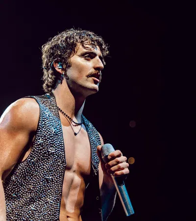 Muscular male singer with curly hair and sleeveless studded vest performing on stage with microphone