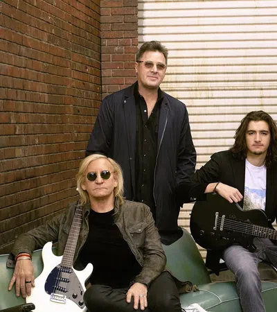 Five male musicians posing with electric guitars in an urban alley with brick walls and a closed metal door.