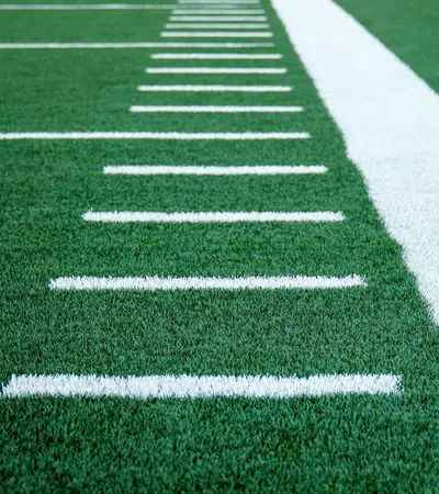 Close-up of green turf with white yard lines on an American football field.