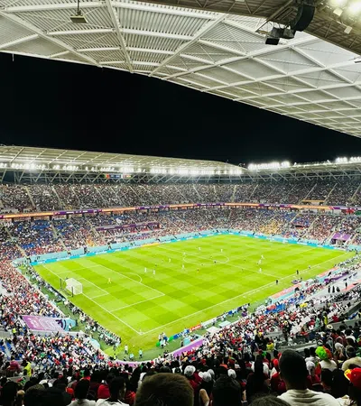 Nighttime soccer match in a packed stadium with bright lights and enthusiastic crowd.