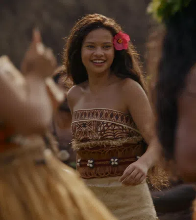 Smiling woman with a flower in her hair dances in traditional Polynesian attire among a group of dancers.