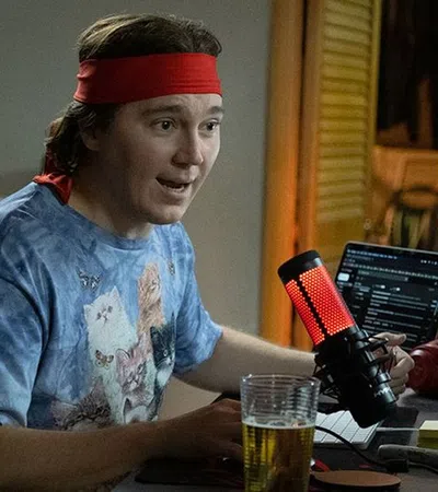 Paul Dano sitting at a desk with a computer and a microphone