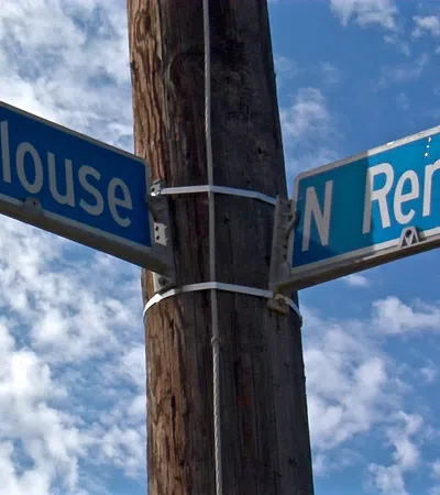 Street signs for Toulouse and N Rendon mounted on a wooden pole against a partly cloudy blue sky.