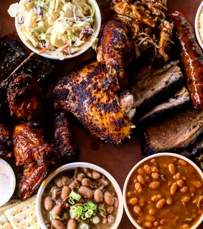 Barbecue feast with smoked chicken, ribs, sausage, brisket, wings, beans, coleslaw, and sides served on a platter.