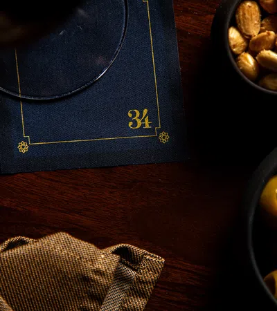 Dark wood table with bowls of green olives and roasted nuts beside a navy blue napkin numbered 34