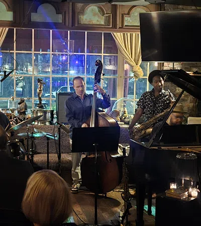 Live jazz band performing with drums, upright bass, saxophone, and piano in cozy pub setting with audience