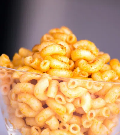Clear glass bowl filled with curly, orange seasoned cheese snacks on a white surface with blurred background