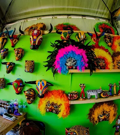 Colorful animal masks and crafts displayed on a bright green wall at an outdoor market stall under a tent.