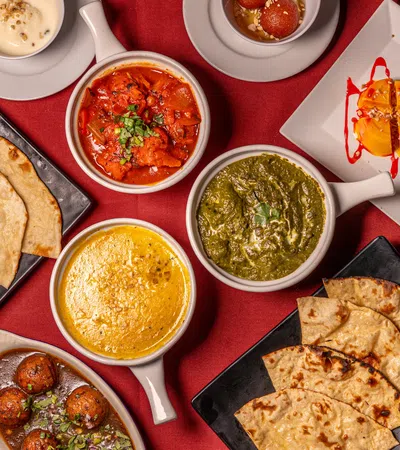 Variety of Indian dishes including naan, curries, gulab jamun, and dessert served on a red tablecloth.