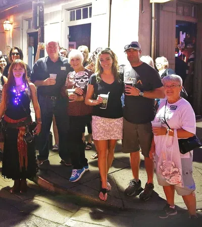 Group of people gathered on a lit street at night holding drinks and smiling, casual and festive atmosphere.