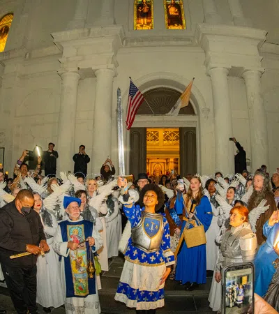 Nighttime religious procession with people in medieval costumes and angel wings outside a historic white church.