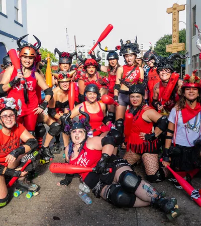 Group of roller derby players in red outfits and helmets posing with red bats on city street during daytime