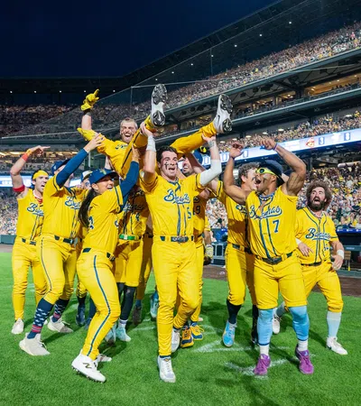 Baseball team in yellow uniforms celebrating on field with fans cheering in stadium at night game