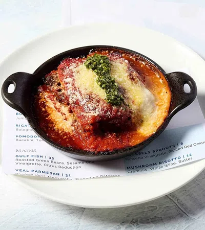 Baked veal parmesan with tomato sauce, cheese, and pesto served in a black dish on a white plate
