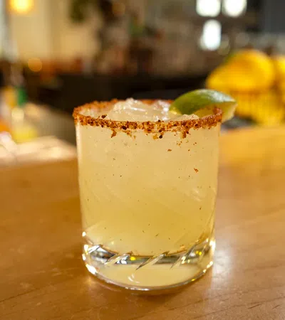 Chilled margarita cocktail with salted rim and lime wedge on wooden bar counter.