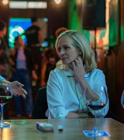 Two people engaged in conversation over wine glasses at a dimly lit bar with blurred background patrons.