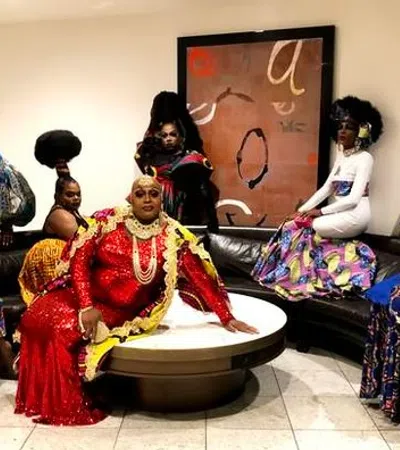 Group of people in colorful, traditional African-inspired attire posing in a modern lounge area around a round table.