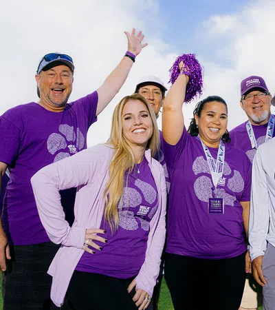 Group of diverse happy people wearing purple event shirts celebrating outdoors with a pom-pom and medals
