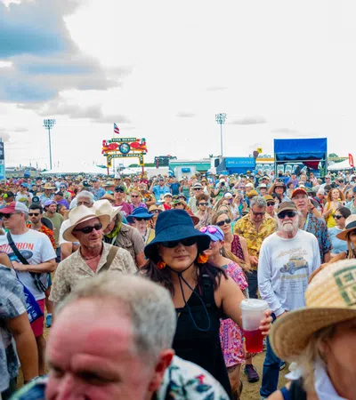 Large diverse crowd at an outdoor festival under a cloudy sky with colorful tents and flags.