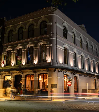 Historic corner building with arched windows illuminated at night with passing car light trails.
