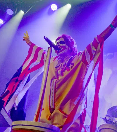 A performer in a vivid clown costume strikes a pose on stage with colorful lighting.