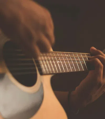 Close-up of hands playing an acoustic guitar with warm lighting and shallow depth of field.
