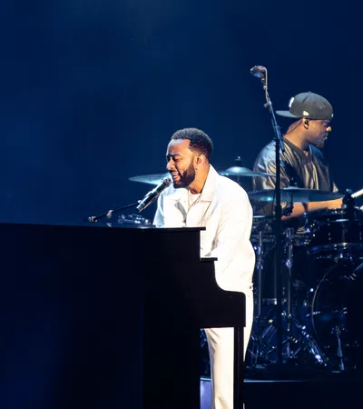 Singer playing piano and drummer performing on stage with dark blue background during concert