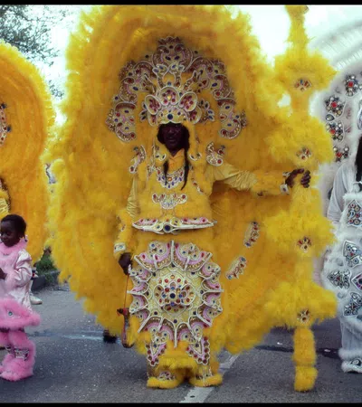 Three people in elaborate yellow and white beaded Mardi Gras costumes with large feathered headdresses stand outdoors