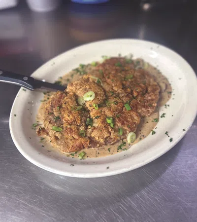 Plate with crispy fried chicken steak covered in creamy gravy and garnished with chopped green onions