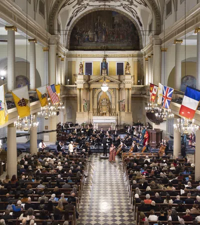 Interior of a historic church filled with an audience attending a musical concert with flags hanging along the walls.