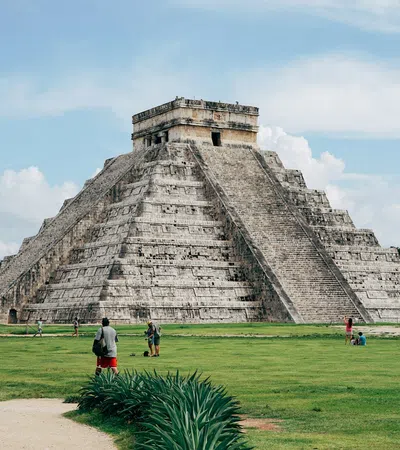 a pyramid with people walking around with Chichen Itza in the background