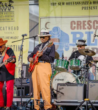 Three musicians performing live on stage at Crescent City Blues and BBQ Festival with guitars and drums.