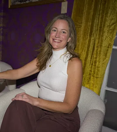 Smiling woman in white sleeveless top sitting in armchair holding a cocktail glass at a marble table